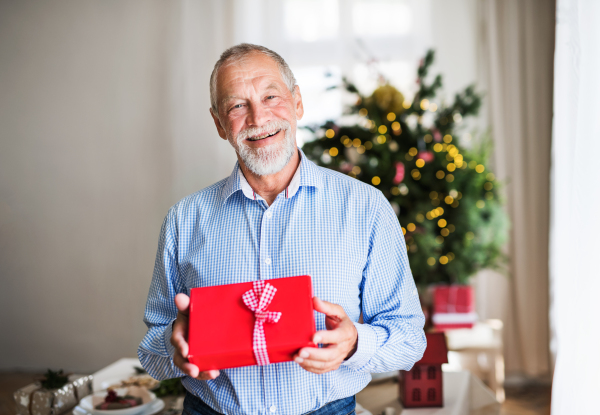 A portrait of a senior man holding wrapped present at Christmas time.