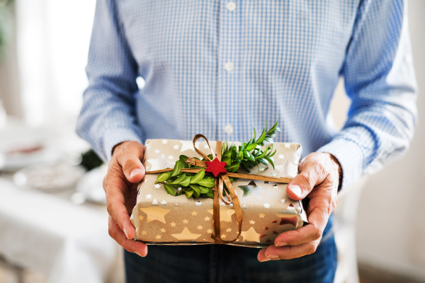 An unrecognizable senior man holding a wrapped present at Christmas time.