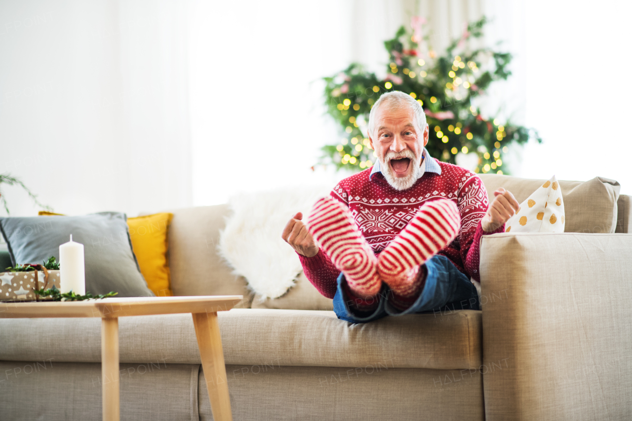 A cheerful senior man with striped red and white socks at home at Christmas time sitting on a sofa, having fun.