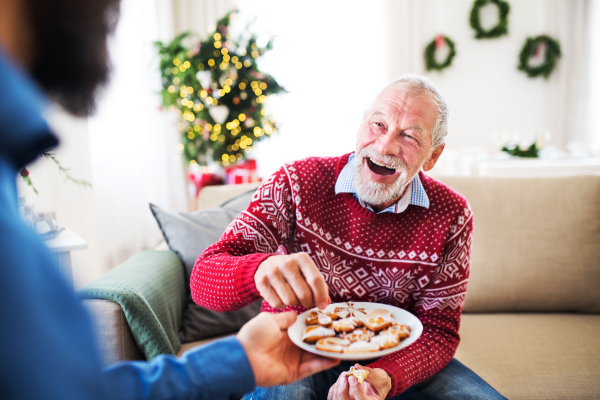 An unrecognizable man giving biscuits to his senior father at home at Christmas time.