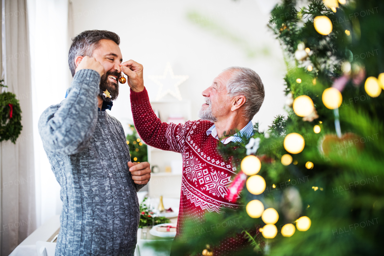 A happy senior father and adult son standing by a christmas tree, having fun.