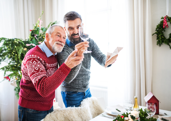 A senior father and adult son setting a table for dinner at Christmas time, talking.