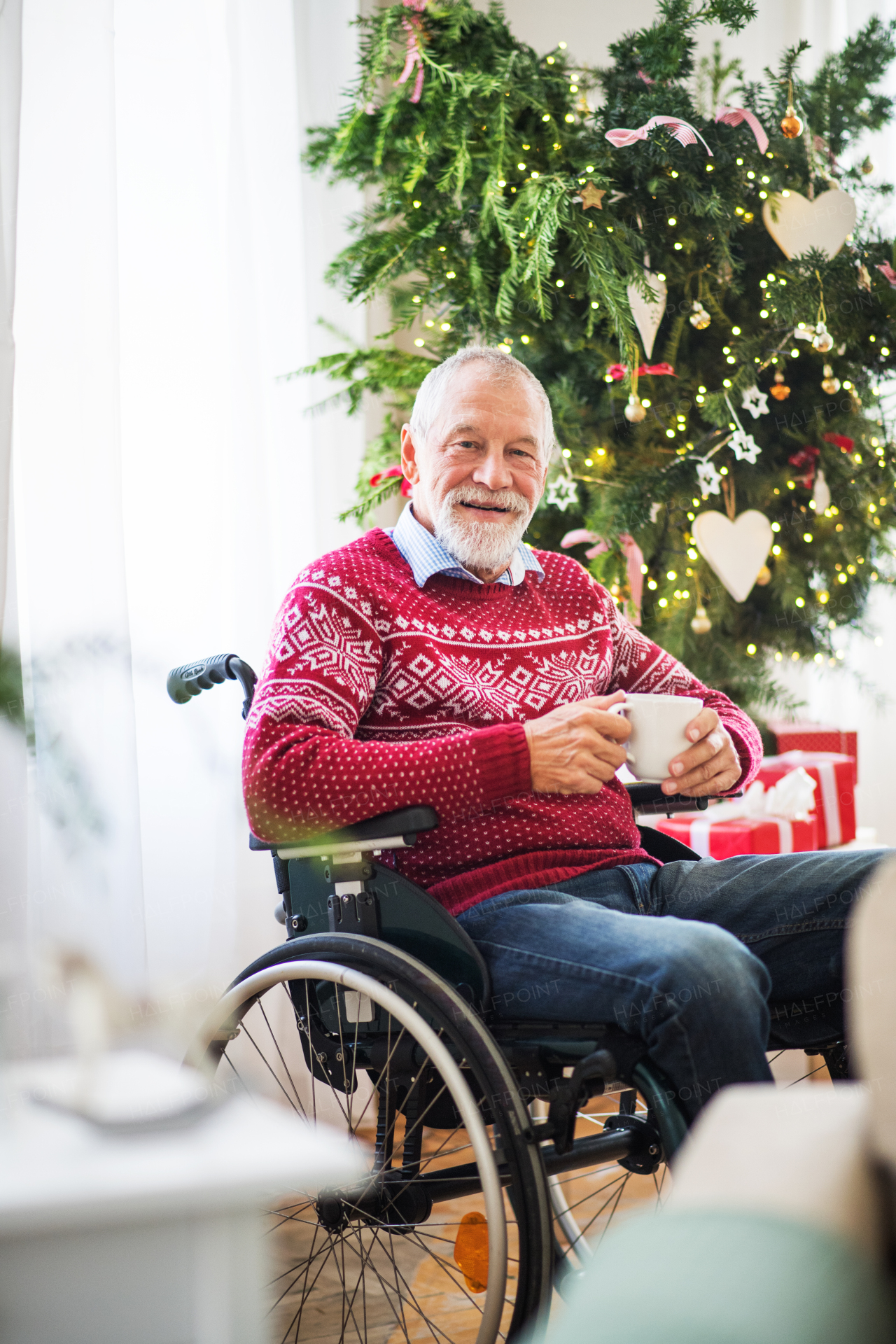 A senior man in wheelchair holding a cup of tea or coffee at home at Christmas time.