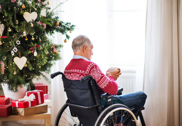 A senior man in wheelchair holding a cup of tea or coffee at home at Christmas time.