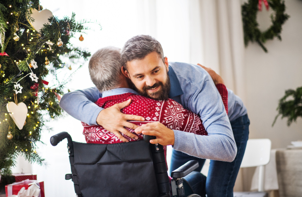 A hipster man hugging his disabled senior father in wheelchair at Christmas time.