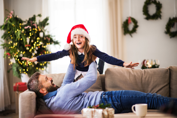 A small girl with Santa hat playing with her father at home at Christmas time, having fun.