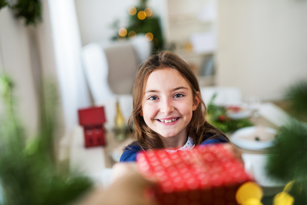 A happy small girl with a present at home at Christmas time.