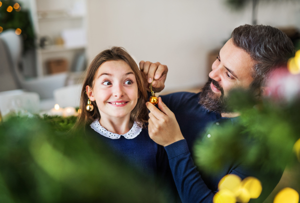 A small girl standing by a Christmas tree with her father at home, having fun.