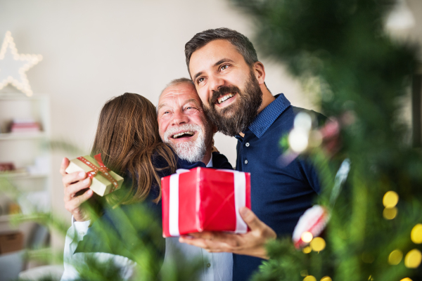 A small girl with father and grandfather exchanging presents at Christmas time, hugging.