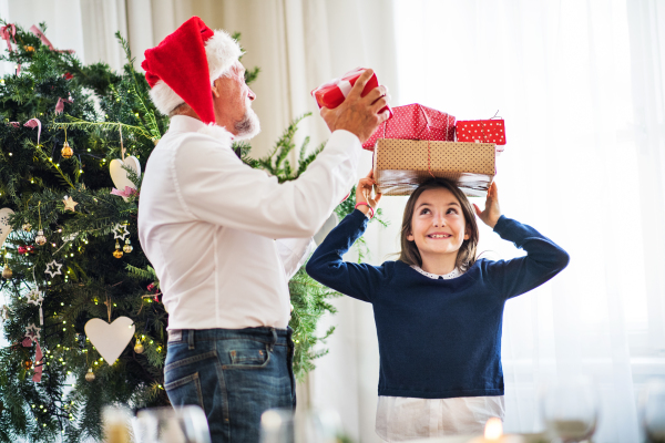 A senior man with a Santa hat and a small girl with presents on her head at Christmas time.