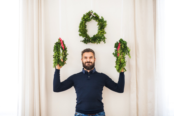 A mature hipster man holding green wreaths at Christmas time, having fun.