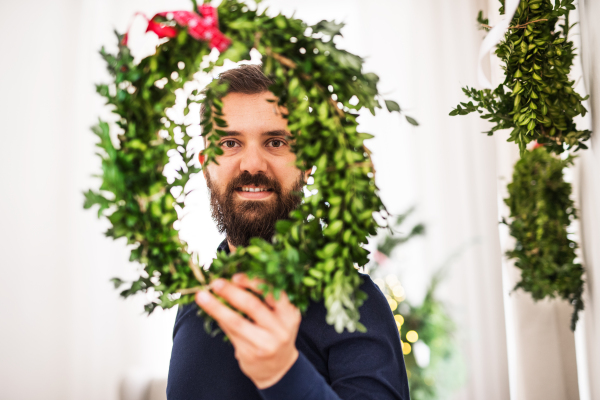 A mature hipster man holding and looking through a green wreath at Christmas time.