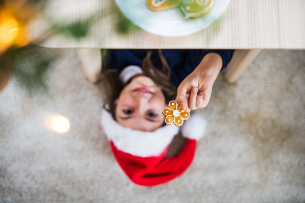 A top view of a small girl with Santa hat lying on the floor at Christmas time, holding biscuit.