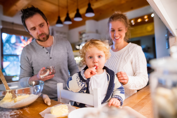 Beautiful young family making cookies at home. Father, mother and a toddler boy baking gingerbread Christmas cookies.