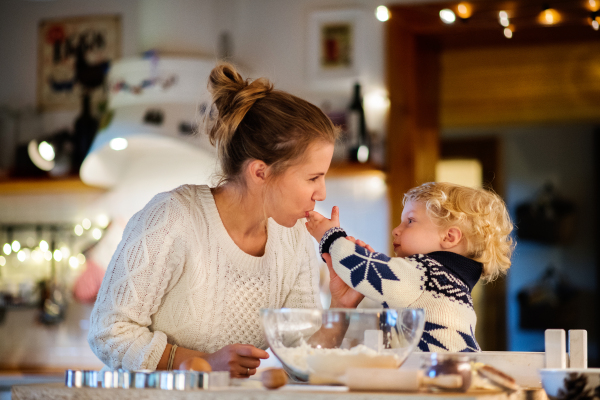 Beautiful young family making cookies at home. Mother and a toddler boy baking gingerbread Christmas cookies.