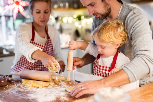 Man, woman and toddler boy making cookies at home. Father, mother and son baking gingerbread Christmas cookies.