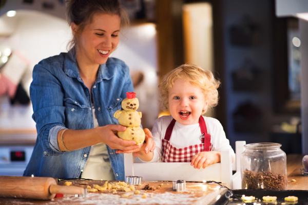 Young woman and toddler boy making cookies at home. Mother and son baking gingerbread Christmas cookies.