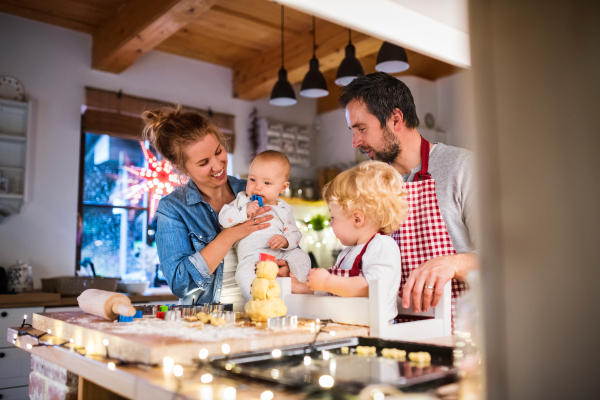 Beautiful young family making cookies at home. Father, mother. toddler boy and baby having fun.