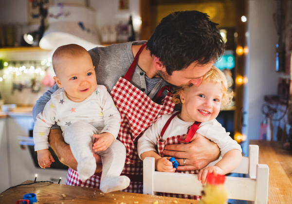 Man with a baby and a toddler boy making cookies at home. Father and son baking gingerbread Christmas cookies.