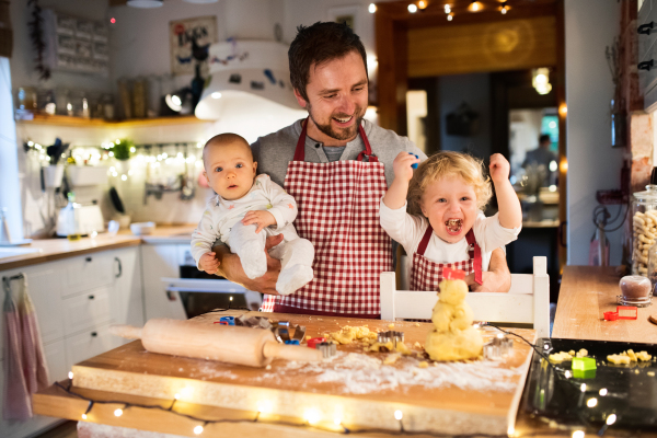 Man with a baby and a toddler boy making cookies at home. Father and son baking gingerbread Christmas cookies.