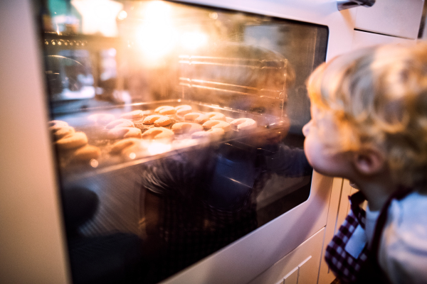 Young family making cookies at home. Unrecognizable toddler boy looking at cookies in the oven. Close up.