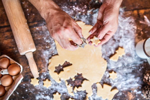 Baking gingerbread cookies at Christmas time. Unrecognizable man cutting out star shapes. High angle view.