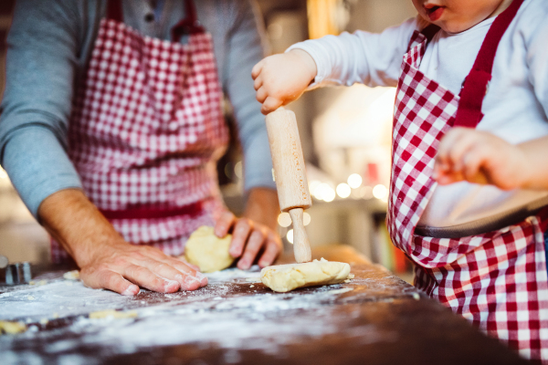 Unrecognizable man and toddler boy making cookies at home. Father and son baking gingerbread Christmas cookies.