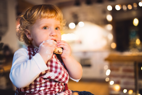 Unrecognizable toddler boy making gingerbread cookies at home. Little boy sitting on the table, eating. Christmas time. Close up.