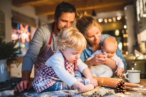 Beautiful young family making cookies at home. Father, mother. toddler boy and baby having fun.