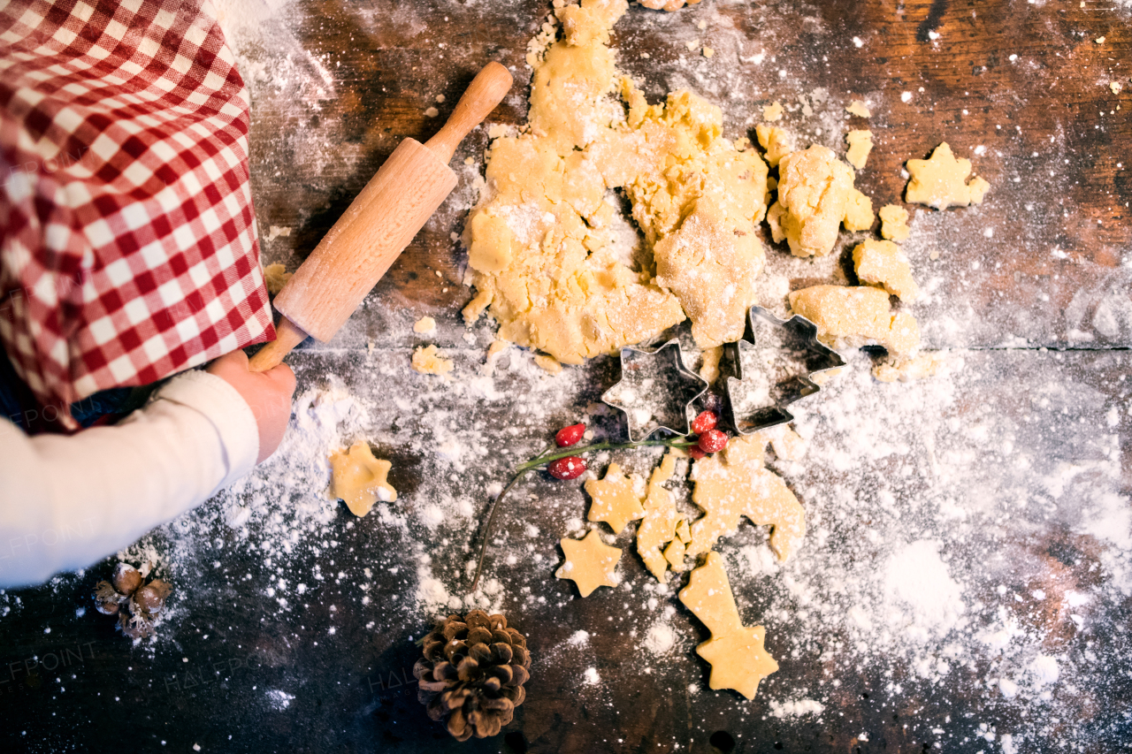 Unrecognizable toddler making gingerbread cookies at home. Little boy sitting on the table. Christmas time. Aerial view.