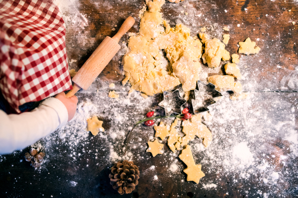 Unrecognizable toddler making gingerbread cookies at home. Little boy sitting on the table. Christmas time. Aerial view.