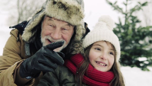 A close-up of a senior grandfather and a small girl having fun in snow on a winter day.