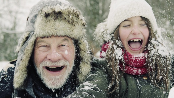 A close-up of a senior grandfather and a small girl having fun in snow on a winter day.