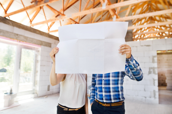 Young married couple or architects or civil engineers looking at plans of the new house, discussing issues at the construction site.