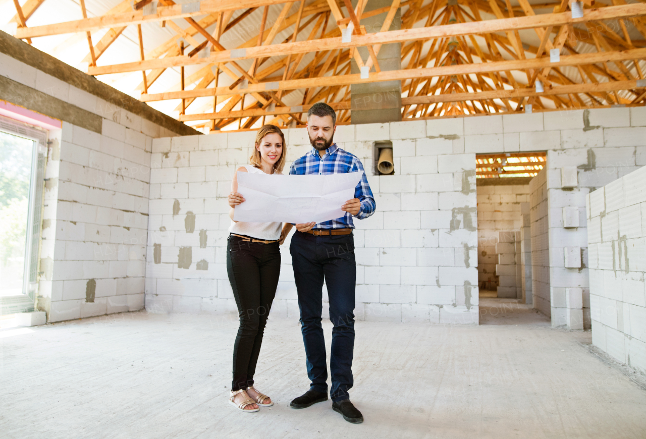 Young couple or architects or civil engineers looking at plans of the new house, discussing issues at the construction site.