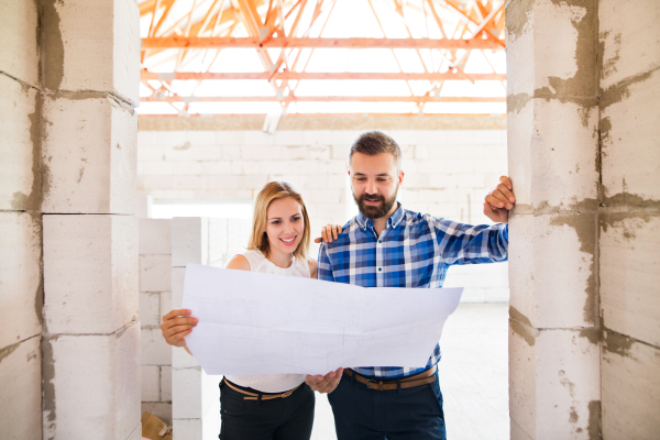 Young couple or architects or civil engineers looking at plans of the new house, discussing issues at the construction site.