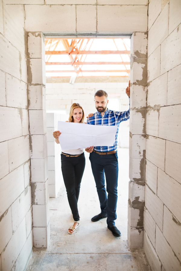 Young couple or architects or civil engineers looking at plans of the new house, discussing issues at the construction site.