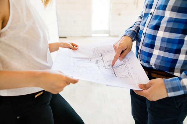 Unrecognizable young couple at the construction site. A man and woman looking at plans of the new house, discussing issues at the construction site.