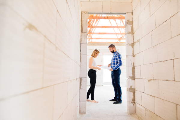 Young couple or architects or civil engineers looking at plans of the new house, discussing issues at the construction site.