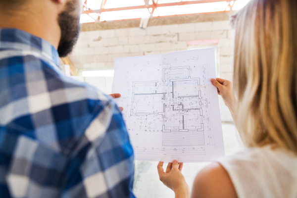 Unrecognizable young couple at the construction site. A man and woman looking at plans of the new house, discussing issues at the construction site.