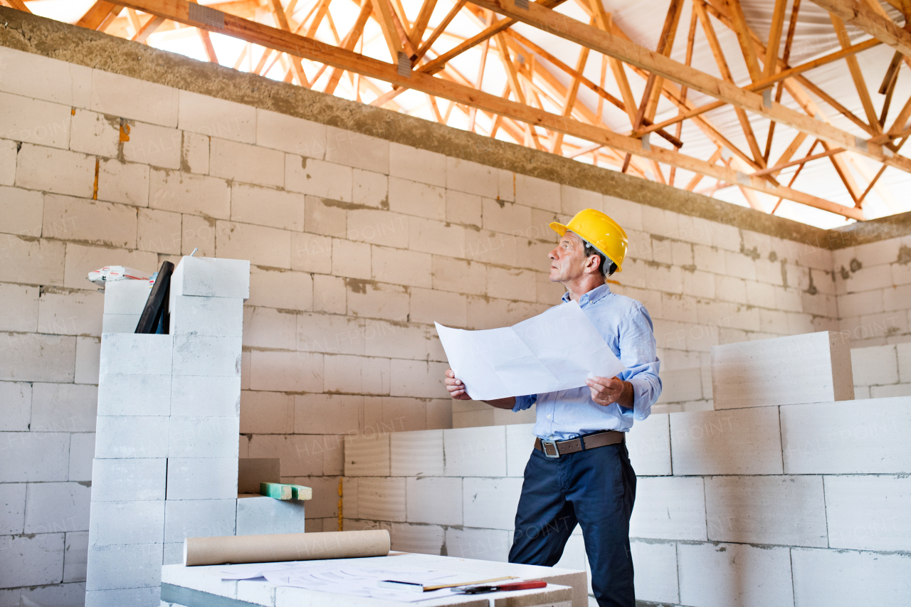 Senior architect or civil engineer at the construction site looking at blueprints, controlling issues at the construction site.