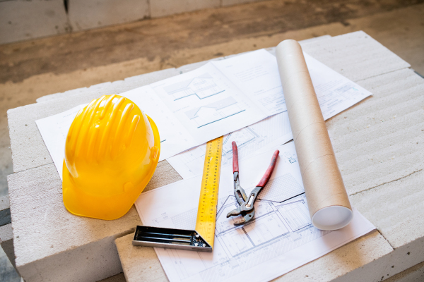 Close up of pliers, square ruler, helmet and blueprints on construction site