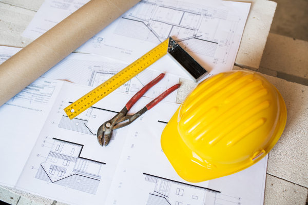 Close up of pliers, square ruler, helmet and blueprints on construction site