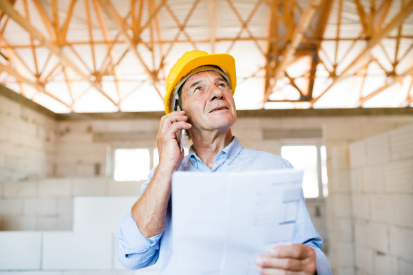 Senior architect with smartphone at the construction site making a phone call.