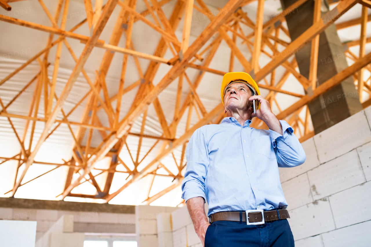 Senior architect with smartphone at the construction site making a phone call.