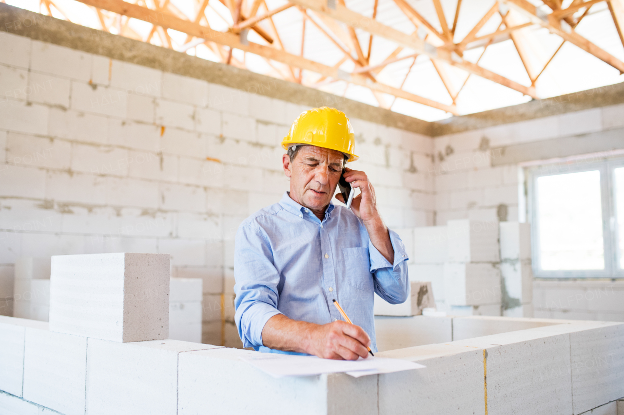 Senior architect with smartphone at the construction site making a phone call.