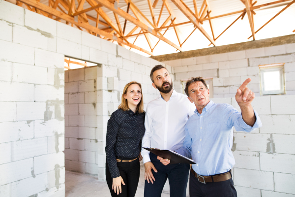 Young couple with architect or civil engineer looking at plans of their new house, discussing issues at the construction site.