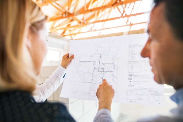 Unrecognizable architects at the construction site, looking at blueprints, controlling issues.