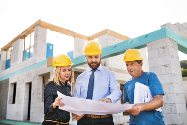 Architect, civil engineer and worker looking at plans and blueprints, discussing issues at the construction site.