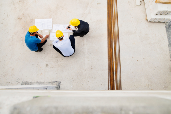 Architect, civil engineer and worker looking at plans and blueprints, discussing issues at the construction site. High angle view.